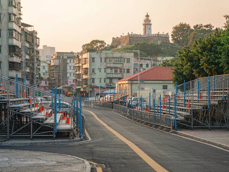 澳门东望洋赛道街景，看台与护栏沿街搭建，远眺东望洋灯塔